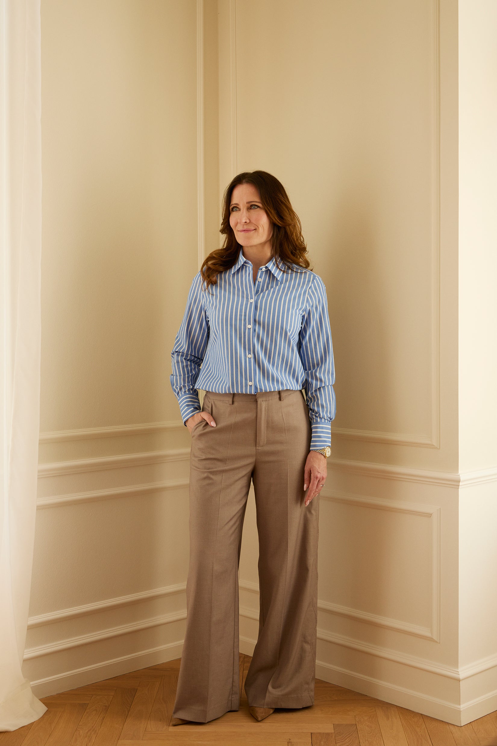 Louise Herping iført Tidløs Skjorte fra A Working Theory i blå- og hvidstribet 100% økologisk bomuld. Klassisk og tidløs skjorte til kvinder med fokus på pasform og funktionalitet, stylet med elegante bukser til en stilren og professionel garderobe.